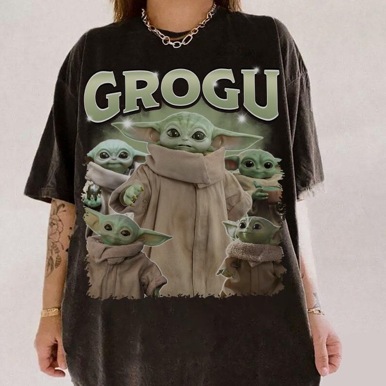May include: Black t-shirt featuring the word "GROGU" in green letters above a graphic of Grogu from The Mandalorian. The graphic shows Grogu in various poses, wearing a tan cloak.