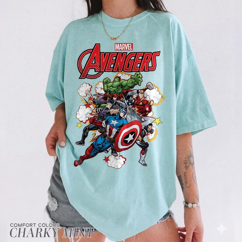 Pu&ograve; includere: Una t-shirt verde menta chiaro con una stampa grafica dei personaggi Marvel Avengers, tra cui Hulk, Captain America e Iron Man. Il testo "MARVEL AVENGERS" &egrave; stampato in rosso e nero sopra la colorata scena d'azione con nuvole bianche.