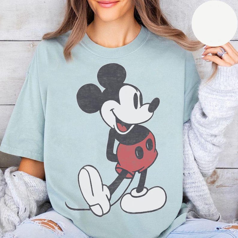 Peut inclure: T-shirt bleu clair avec un motif de Mickey Mouse. Le personnage de dessin anim&eacute; est en noir, blanc et rouge, souriant. Le t-shirt a une coupe ample et des manches courtes, adapt&eacute; aux tenues d&eacute;contract&eacute;es. Un classique.