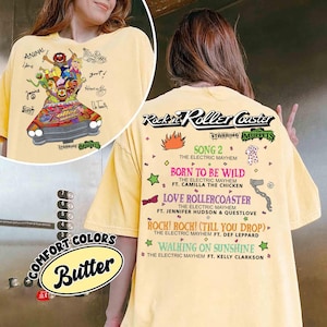 May include: Pale yellow t-shirt with a Muppets-themed graphic of a roller coaster and characters, with text including "Rockin' Roller Coaster" and song titles. The shirt also has the words "Comfort Colors" and "Butter".