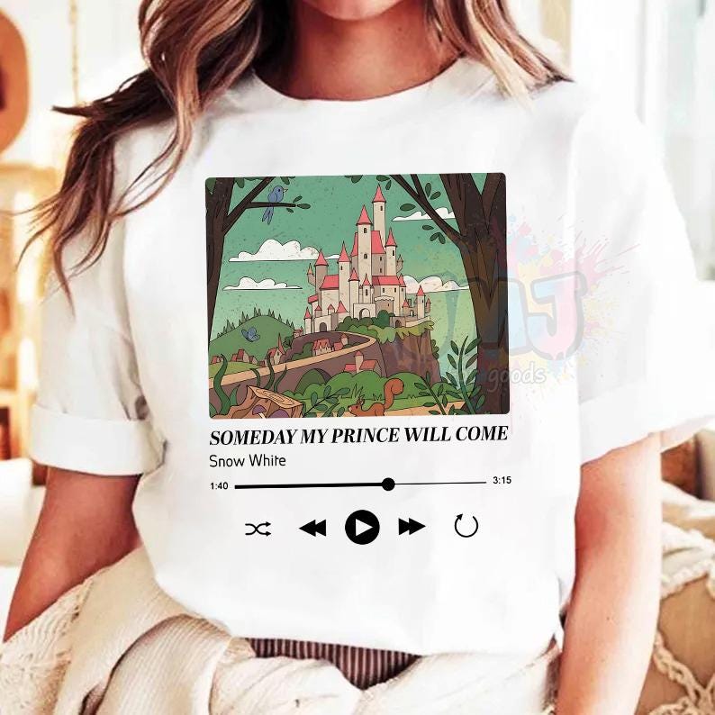 May include: A white t-shirt featuring a rectangular graphic of a castle on a hill surrounded by trees. Below the illustration, the text reads: SOMEDAY MY PRINCE WILL COME, Snow White, with a music player progress bar and playback control icons.