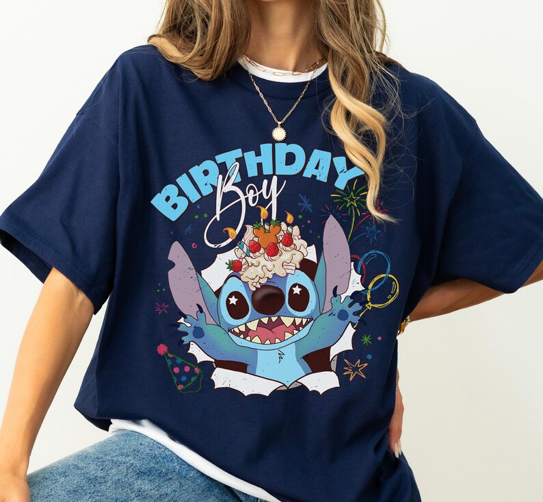 K&ouml;nnte beinhalten: Marineblaues T-Shirt mit einem Cartoon-Charakter und dem Text "BIRTHDAY Boy". Die Figur hat einen Geburtstagskuchen auf dem Kopf. Das Design umfasst Feuerwerk, Luftballons und eine Partyh&uuml;tchen.