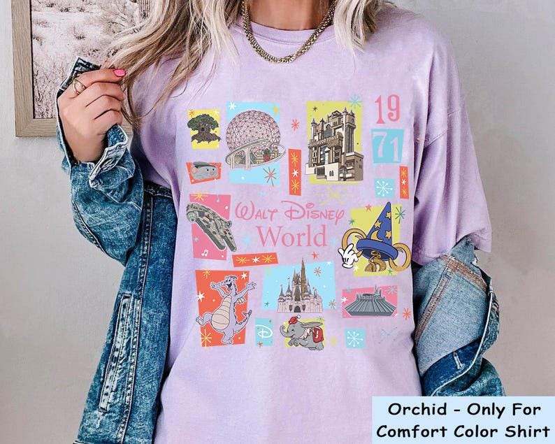 May include: Orchid-colored t-shirt with a colorful graphic design featuring various Walt Disney World icons, including the Millennium Falcon, Cinderella's Castle, and the Sorcerer's Hat. The text "Walt Disney World" and the year "1971" are also displayed.