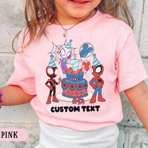 Op de afbeelding: Roze T-shirt met een verjaardagstaart met het nummer 7 en Spider-Man-personages. Het shirt heeft de tekst "CUSTOM TEXT" onder de taart. Het shirt is roze.