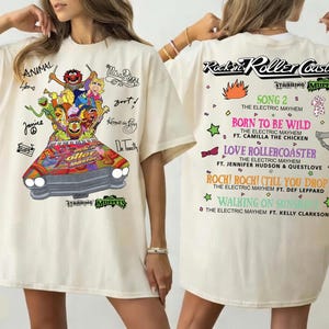 May include: Ivory t-shirt with a colourful graphic of the Muppets in a car and the text "Rockin' Roller Coaster". The back of the shirt lists song titles and artist names. The shirt is a short-sleeved, oversized style.