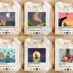 May include: Six off-white t-shirts featuring rectangular graphic prints of animated scenes with song titles, character names, and music player interface icons. Each shirt displays a unique illustration, including a pumpkin carriage, floating lanterns, a cliffside figure, a boat, a mermaid on a rock, and a warrior figure.