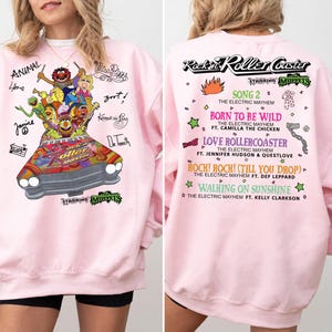 May include: Pink sweatshirt with a Muppets graphic on the front, including characters in a car. The back displays "Rockin' Roller Coaster" and song titles. The long-sleeved sweatshirt is a casual garment.