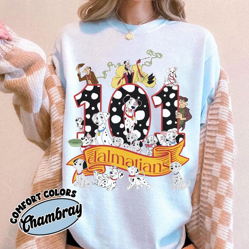 May include: Light blue sweatshirt featuring a graphic of the number 101 with Dalmatian dogs and characters from the Disney movie. The word "Dalmatians" is on a yellow banner. The sweatshirt has the words "Comfort Colors Chambray" on the bottom left.