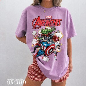 Pu&ograve; includere: Una t-shirt a maniche corte color viola chiaro con una stampa grafica dei personaggi Marvel Avengers, tra cui Hulk, Captain America e Iron Man. Il testo Marvel Avengers &egrave; stampato in rosso e bianco sopra i personaggi sul davanti.