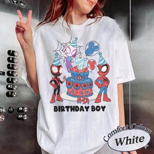 Op de afbeelding: Wit T-shirt met een kleurrijke afbeelding van Spider-Man-personages, een verjaardagstaart en de tekst "BIRTHDAY BOY". Het ontwerp bevat een Spider-Man-logo en een kaars met nummer 7. Het shirt heeft ook de tekst "Comfort Colors White".