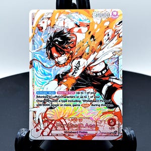 Puede incluir: Una carta coleccionable holográfica con una ilustración de Portgas D. Ace con llamas naranjas, pantalones cortos negros y un tatuaje en el brazo. La carta muestra el texto Portgas D. Ace, Whitebeard Pirates y reglas en inglés.