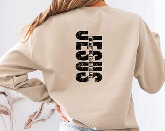 May include: Sand-colored sweatshirt with the word "JESUS" printed vertically in distressed black font on the back. Below the word "JESUS" is the text "THE WAY THE TRUTH THE LIFE". The word "SAND" is printed at the bottom.