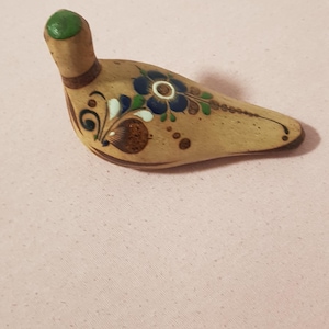 Può includere: Statuetta di uccello in ceramica fatta a mano. L'uccello è color beige con disegni floreali blu, bianchi e marroni. La testa è verde. La statuetta è lunga circa 10 cm.