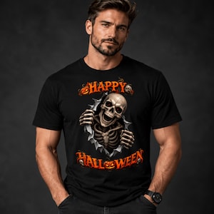 Puede incluir: Una camiseta negra con un gráfico de un esqueleto emergiendo de un efecto de tela rasgada. El diseño incluye el texto naranja "HAPPY HALLOWEEN" con pequeñas ilustraciones de calaveras y calabazas situadas arriba y abajo del esqueleto.