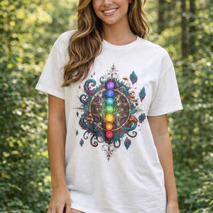 May include: White t-shirt featuring a colorful, intricate design of a geometric pattern with seven colored circles, surrounded by swirling lines and botanical elements. The design is centered on the shirt, creating a visually striking graphic.