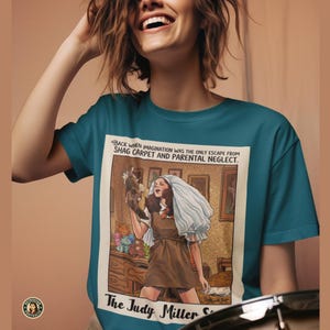 May include: Teal crew neck t-shirt featuring a vintage-style illustration. The graphic depicts a woman in a brown dress and white veil, holding a stuffed animal. Text on the shirt reads "BACK WHEN IMAGINATION WAS THE ONLY ESCAPE FROM SHAG CARPET AND PARENTAL NEGLECT."
