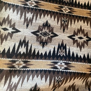 May include: A close-up of a woven rug with a geometric pattern in shades of brown, black, and white. The pattern features triangles, diamonds, and stars.