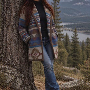 May include: A long-sleeved open-front coat featuring a geometric pattern in shades of blue, brown, and cream. The coat is worn over a black turtleneck jumper and blue denim jeans, paired with brown lace-up hiking boots.