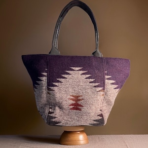 May include: A purple and white tote bag with a geometric pattern. The bag has black leather handles and a zipper closure.