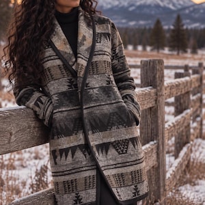 May include: A long-sleeved coat featuring a multi-colored geometric pattern in shades of gray, black, and tan. The coat has a shawl collar, a black trim along the front opening, and two side pockets. It is worn over a black turtleneck and black pants.