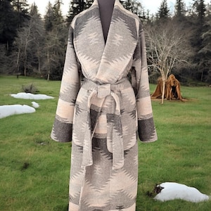 May include: A long, patterned robe in shades of grey and beige, displayed on a mannequin. The robe features a shawl collar, a matching belt, and a geometric design. The robe is made of a thick material, suitable for cooler weather.