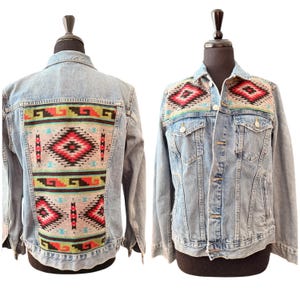 Può includere: Una giacca di jeans blu chiaro con un motivo geometrico colorato sul retro e sul davanti. Il motivo è in tonalità di rosso, nero, verde e blu.
