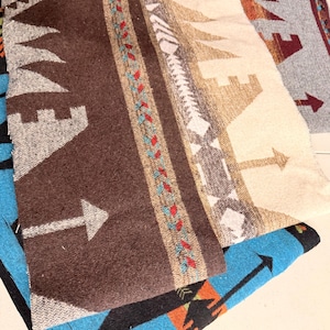 May include: Close-up of several woven blankets with Southwestern designs. The blankets feature brown, blue, grey, and cream colours with arrow and geometric patterns. One blanket has a brown background with a white arrow.
