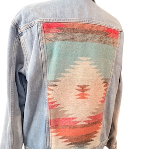 Può includere: Giacca di jeans azzurra con un pannello posteriore fantasia in stile sud-ovest. Il motivo presenta forme geometriche nei toni del rosso, turchese, arancione e crema. La giacca ha un colletto classico, bottoni e tasche.