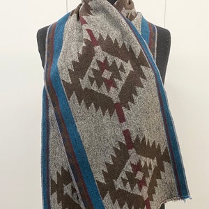 Könnte beinhalten: Ein grauer, brauner und blauer gemusterter Schal mit geometrischem Design. Der Schal ist gefaltet und über eine schwarze Schaufensterpuppe gelegt.