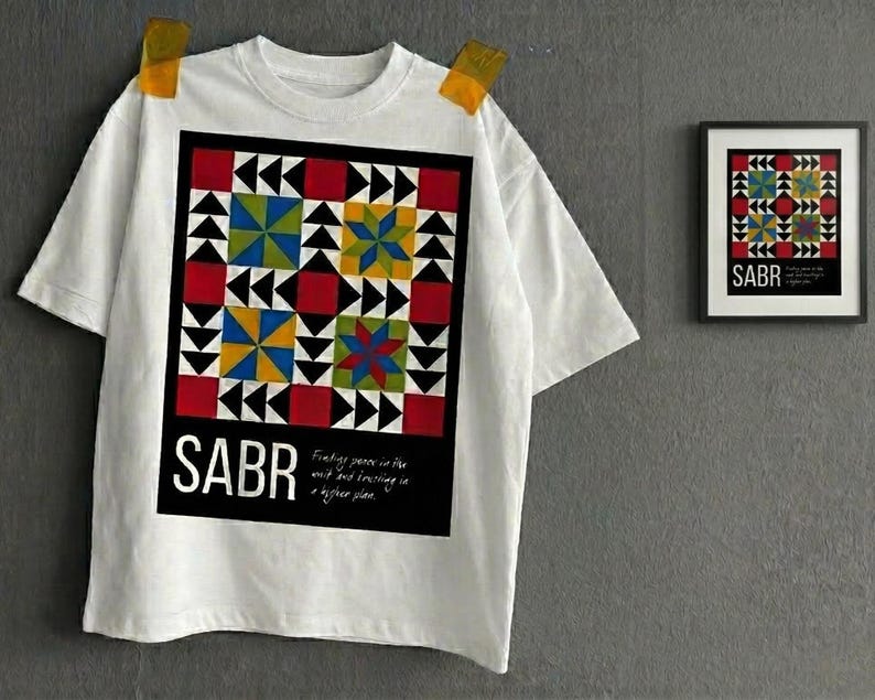May include: White t-shirt with a colorful geometric design featuring red, blue, yellow, and green shapes. The word "SABR" is printed in large white letters at the bottom of the design. A framed print with the same design is on the right.