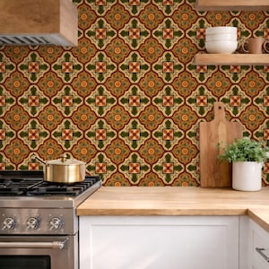 May include: Kitchen scene with a patterned backsplash in shades of green, red, and gold. A stainless steel stove with a gold pot sits in front of the backsplash. Wooden shelves hold white bowls, mugs, a cutting board, and a potted plant.