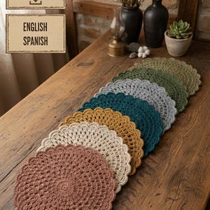 May include: A selection of handmade crochet placemats in shades of brown, beige, gold, teal, grey, and green, displayed on a weathered wooden table. The circular placemats feature a scalloped edge. The image also includes text that says "INSTANT DOWNLOAD" and "ENGLISH SPANISH".