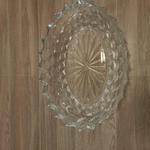 Puede incluir: Fuente ovalada de vidrio transparente con un patrón geométrico texturizado. La fuente tiene un diseño de estrella en el centro y un borde festoneado. La fuente es de vidrio transparente.