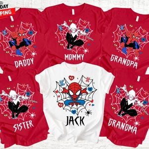 Op de afbeelding: Rode en witte t-shirts met Spider-Man en Spider-Gwen ontwerpen. De shirts zijn gelabeld met "Daddy", "Mommy", "Grandpa", "Sister", "Jack" en "Grandma". De shirts hebben een spinnenwebontwerp met harten en spinnen.