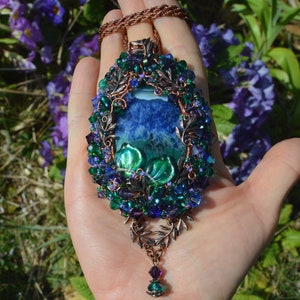 Blue and green fairy pendant wire wrapped with crystals and beads. Tiny copper leaves hang beneath. Wire wrapping is covered with tiny blue purple and green glass cystals, glittering in the light. Central agate is rich marbled blue and green.