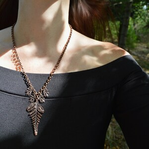 Puede incluir: Un collar de cobre con un colgante de helecho. El collar lo lleva un maniqu&iacute; con un top negro de hombros descubiertos.