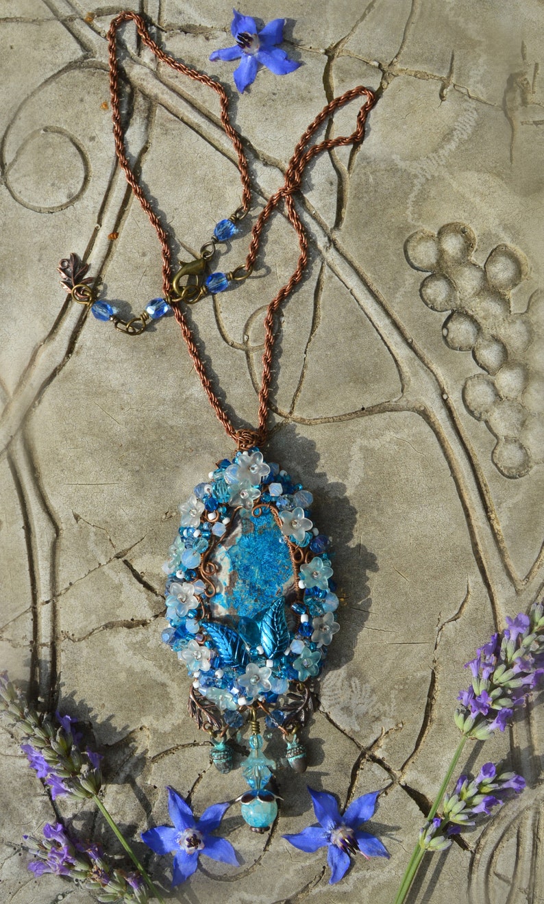 Blue pendant displayed flat on a table. Very long chain shown, with lobnster clasp fastening and adjustable chain with blue beads.