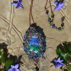 Purple crystal fairy pendant wire wrapped in copper, blue, and green crystals. Oval shaped, 4 inches long and hangs from a copper adgustable chain. Sunlight shows the rich colors and marbled effect of the central agate stone - sapphire blue and green