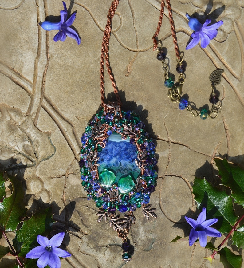 Purple crystal fairy pendant wire wrapped in copper, blue, and green crystals. Oval shaped, 4 inches long and hangs from a copper adgustable chain. Sunlight shows the rich colors and marbled effect of the central agate stone - sapphire blue and green