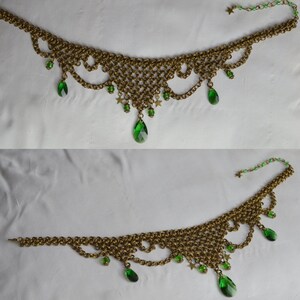May include: A gold-toned chainmail necklace with green teardrop-shaped and star-shaped accents. The necklace features a delicate, lacy design with multiple green gems hanging from the bottom edge. The chain extends to a clasp with additional green beads and a star.