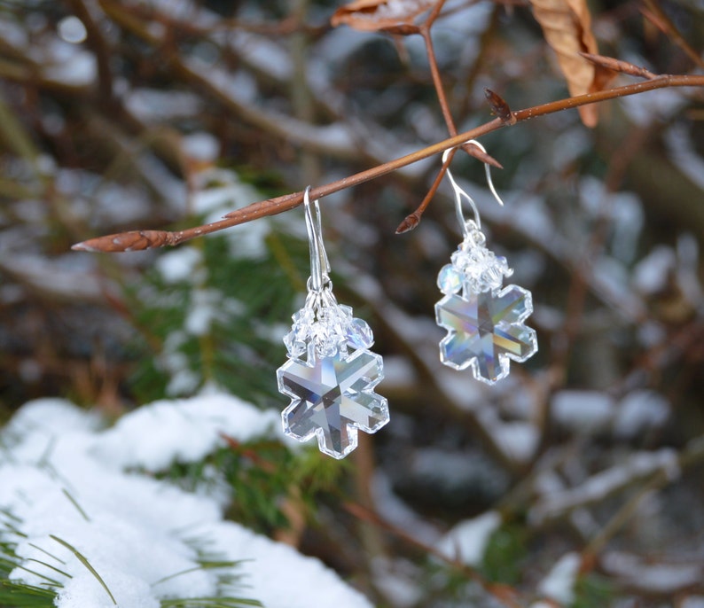 Crystal snowflake earrings showing the refraction and scattered light within the glass. Central snowflakes are large and clear, yet all details and facets are visible. Smaller clear crystals dangling above scatter the light and appear blinding white.
