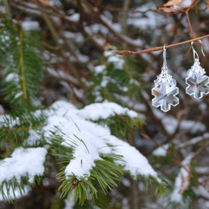 Crystal snowflakes against winter leaves. The crystals are clear, but the facets are reflecting the light to best show how the arge central snowflakes are made of 3 dimensional fine crystal glass.