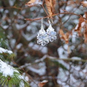 Earrings made of snowflake crystals against snowy landscape. The crystal earrings are clear, yet refract light to appear white in places, glittering and changing as they move. The effect is magical and fairylike.