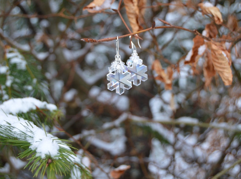 Earrings made of snowflake crystals against snowy landscape. The crystal earrings are clear, yet refract light to appear white in places, glittering and changing as they move. The effect is magical and fairylike.