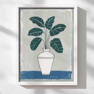 May include: A framed art print featuring a stylized illustration of a houseplant in a white vase. The plant has large, dark green leaves. The background is a light gray with a blue stripe at the bottom. The artwork is in a white frame.