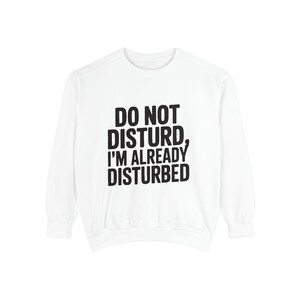 May include: A white long-sleeve sweatshirt featuring the black printed text DO NOT DISTURB, I'M ALREADY DISTURBED centered on the chest. The garment has a crew neckline, ribbed cuffs, and a ribbed hem, providing a clean and simple aesthetic.