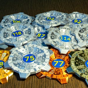 May include: A collection of metallic tokens with various numbers in blue circles. The tokens are in silver, gold, and bronze colors. The numbers range from 75 to 118. The tokens have a star-like design.