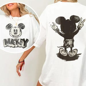 May include: White t-shirt featuring a black and white Mickey Mouse graphic on the front and back. The front graphic includes the word "Mickey". The back graphic shows Mickey Mouse with his arms up in a rock and roll pose.