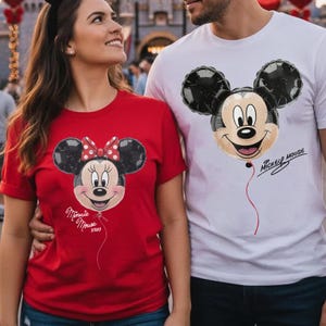 May include: A red t-shirt featuring a Minnie Mouse balloon graphic with a red and white polka dot bow and the text Minnie Mouse xoxo, and a white t-shirt featuring a Mickey Mouse balloon graphic with the text Mickey Mouse in black script.