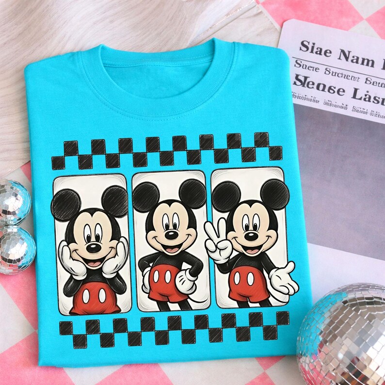 May include: A turquoise blue t-shirt featuring a graphic of Mickey Mouse in three different poses. Each Mickey Mouse is framed in a white rectangle with a black and white checkered border. Mickey is wearing red shorts and white gloves.